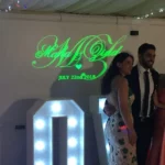 4 people looking at the camera smiling as they get married infront of a custom projected name