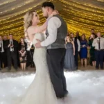 a wedding venue. the background is white and gold lit and has people dancing